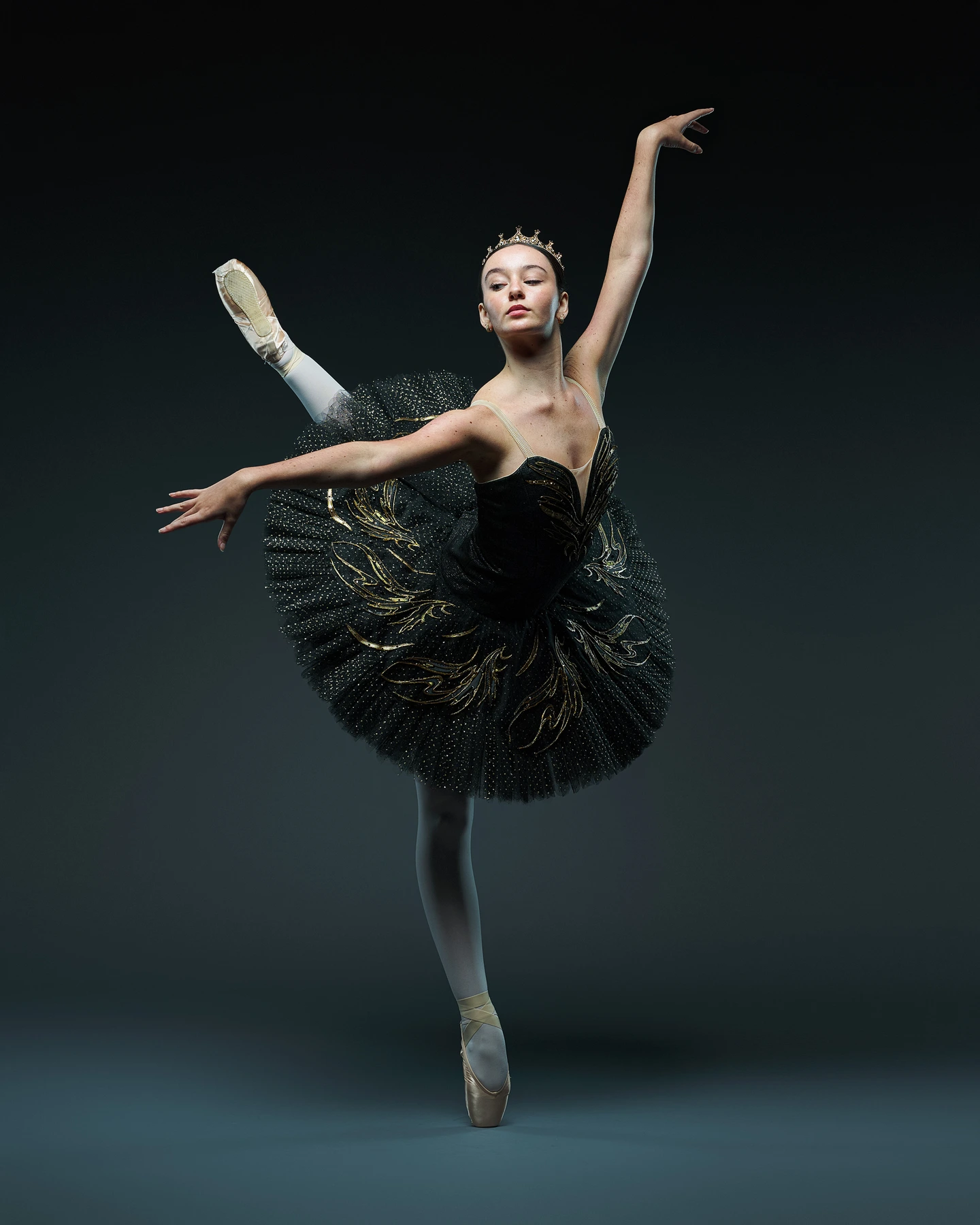 Ballet dancer in an embroidered black and gold tutu, extending her leg in arabesque