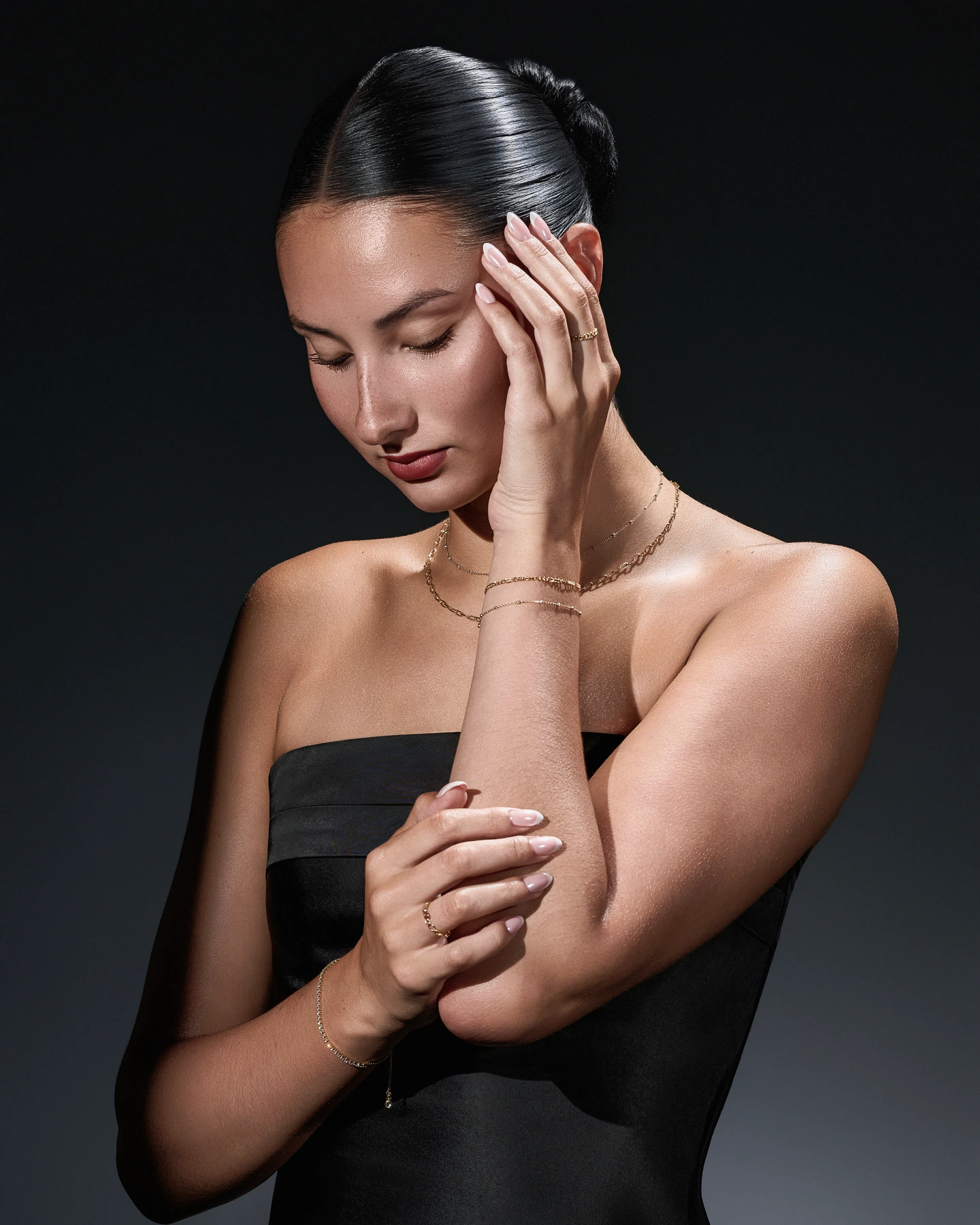 Model wearing layered gold necklaces, bracelets, and rings against a dark backdrop
