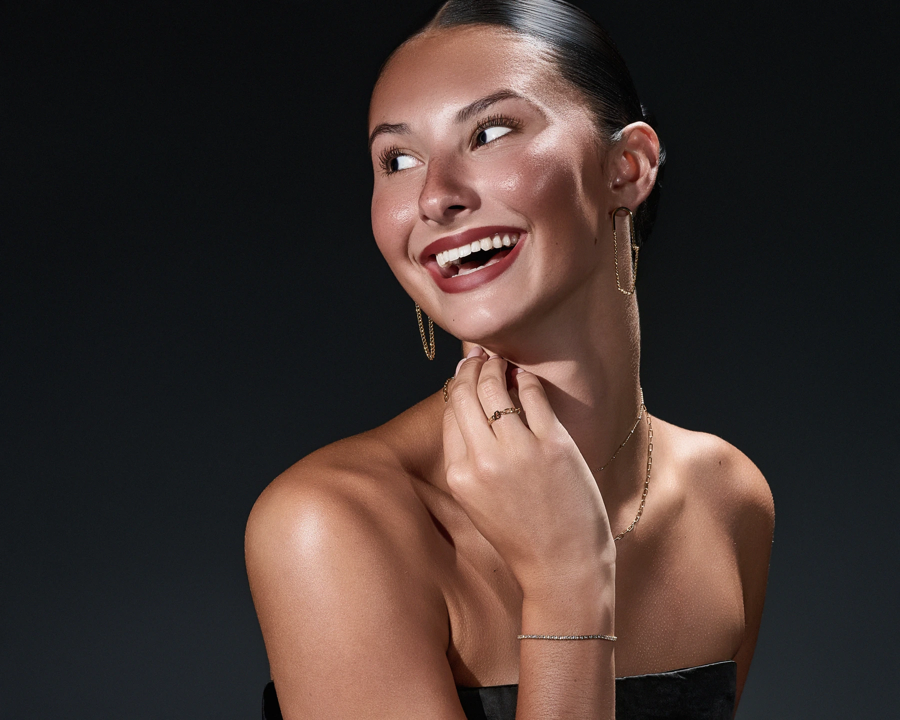 Smiling model wearing long gold earrings and delicate gold necklaces