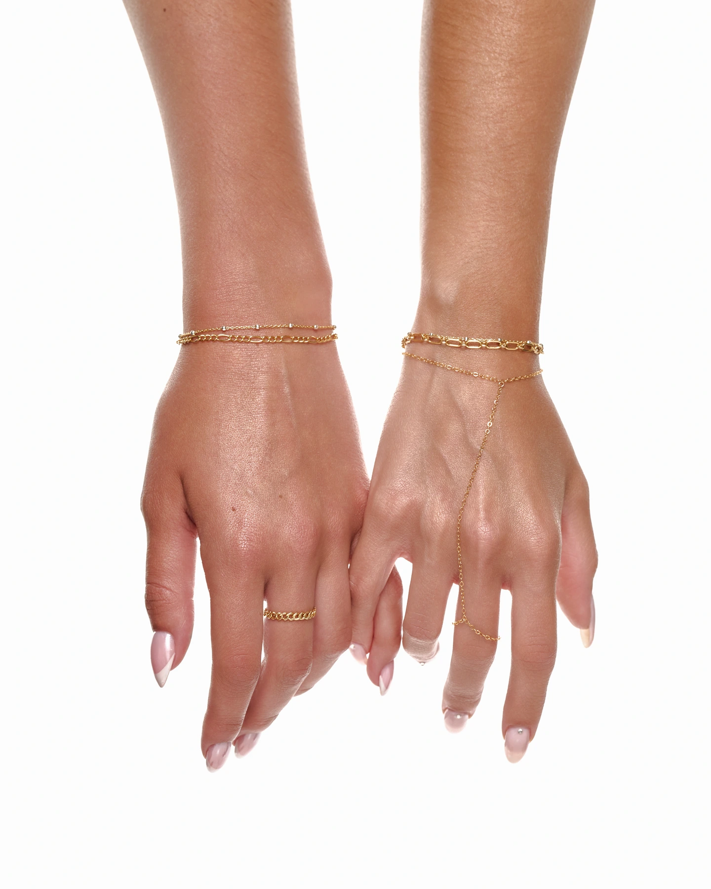 Close-up of gold bracelets, rings, and a delicate hand chain