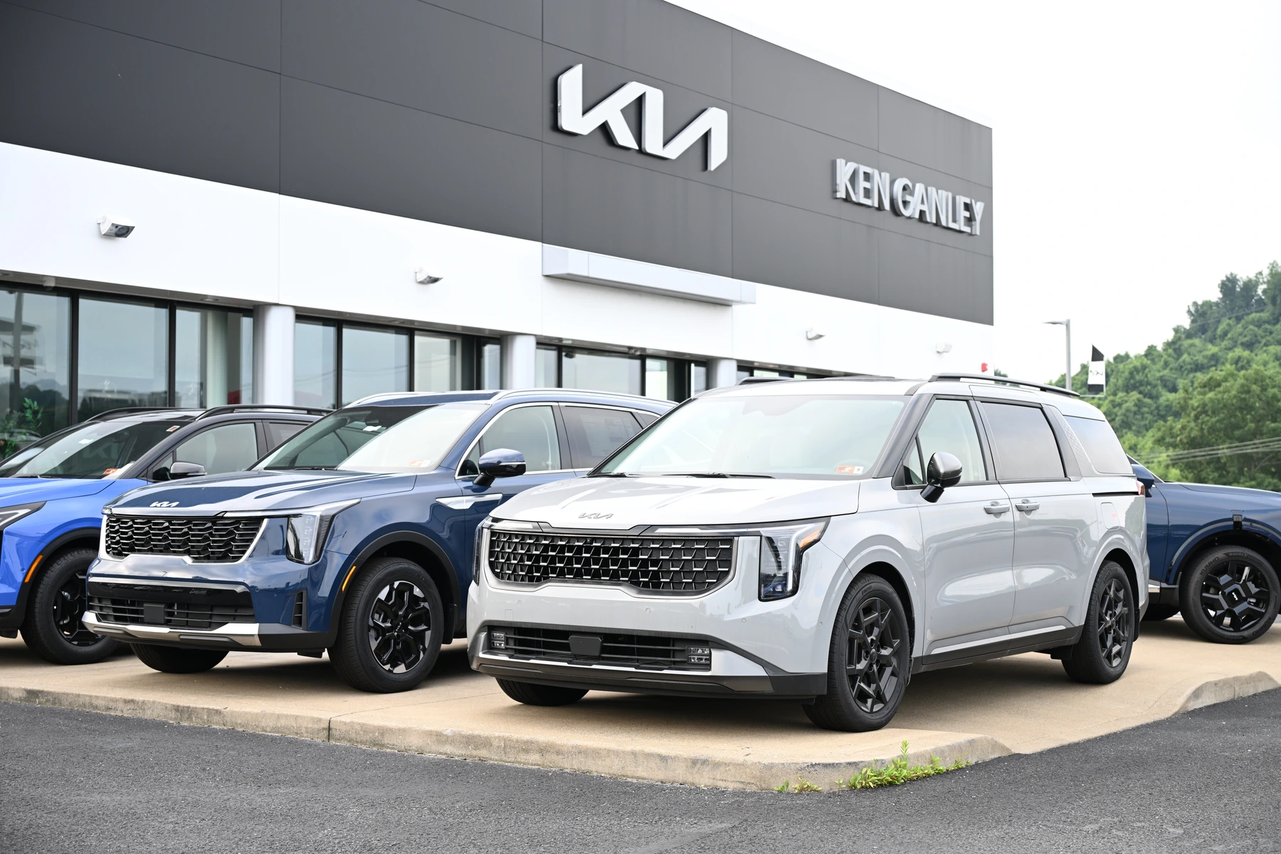 White Kia minivan and blue SUV outside the Ken Ganley Kia showroom