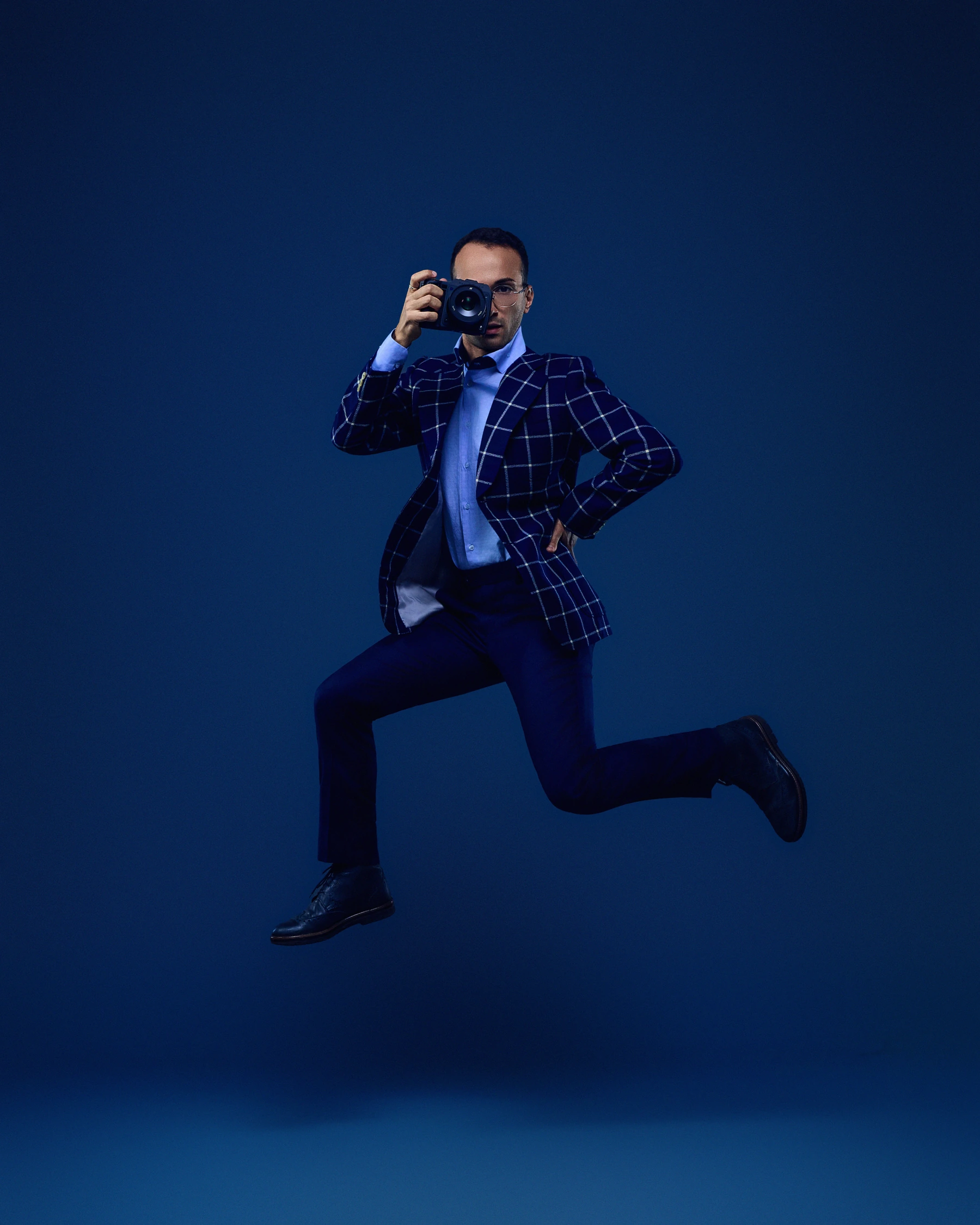 Luca leaping with his camera in a blue suit against a blue studio backdrop