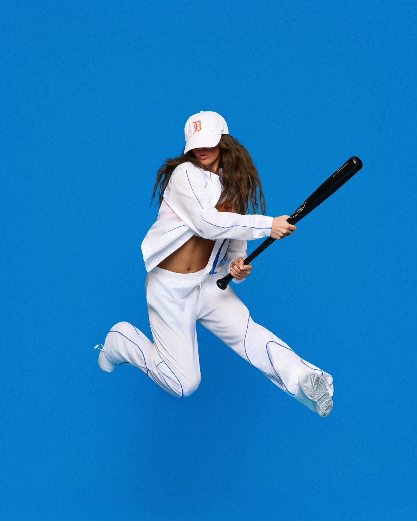 Dancer leaping in a white baseball outfit against vivid blue