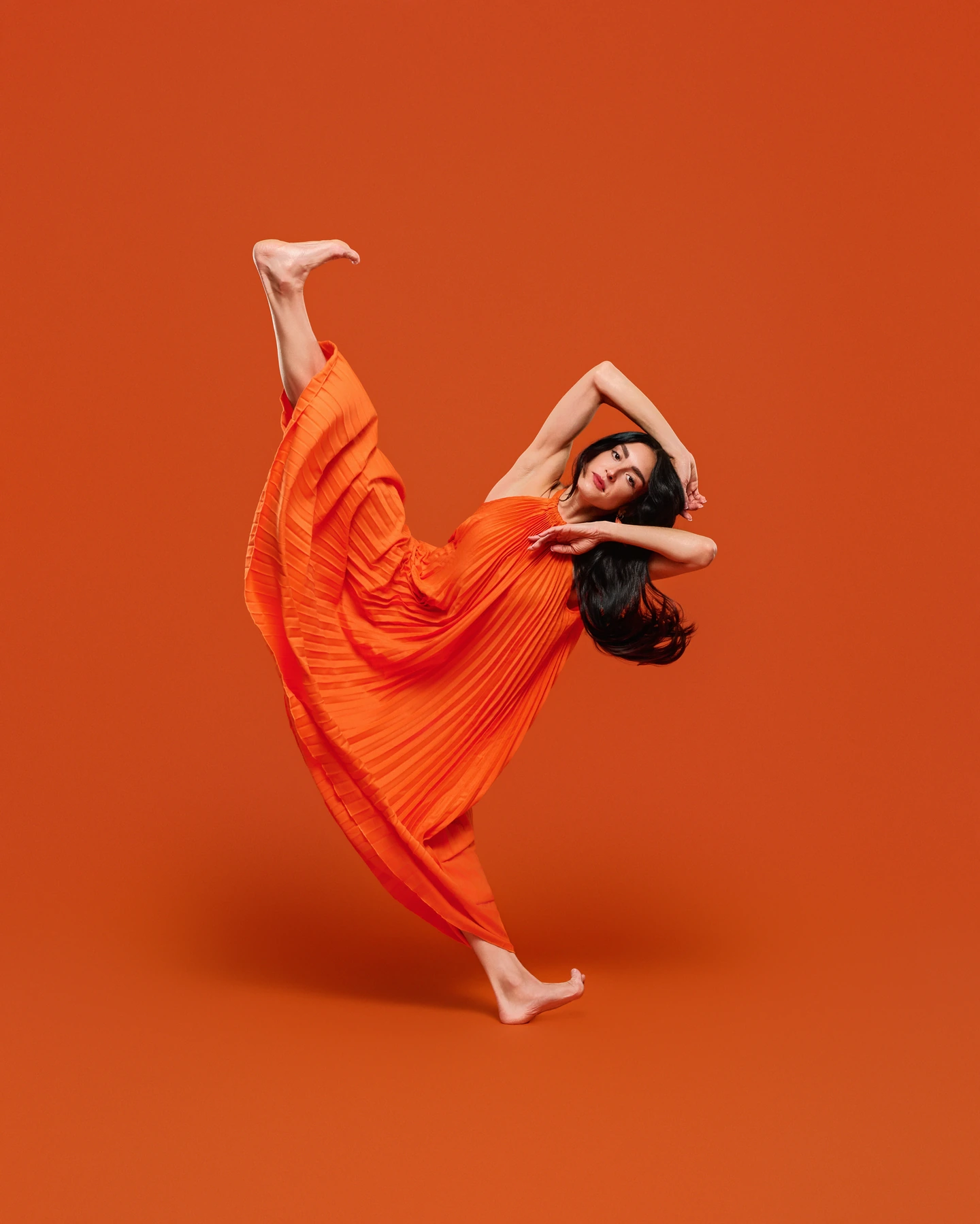 Dancer extending one leg in a flowing orange dress against orange