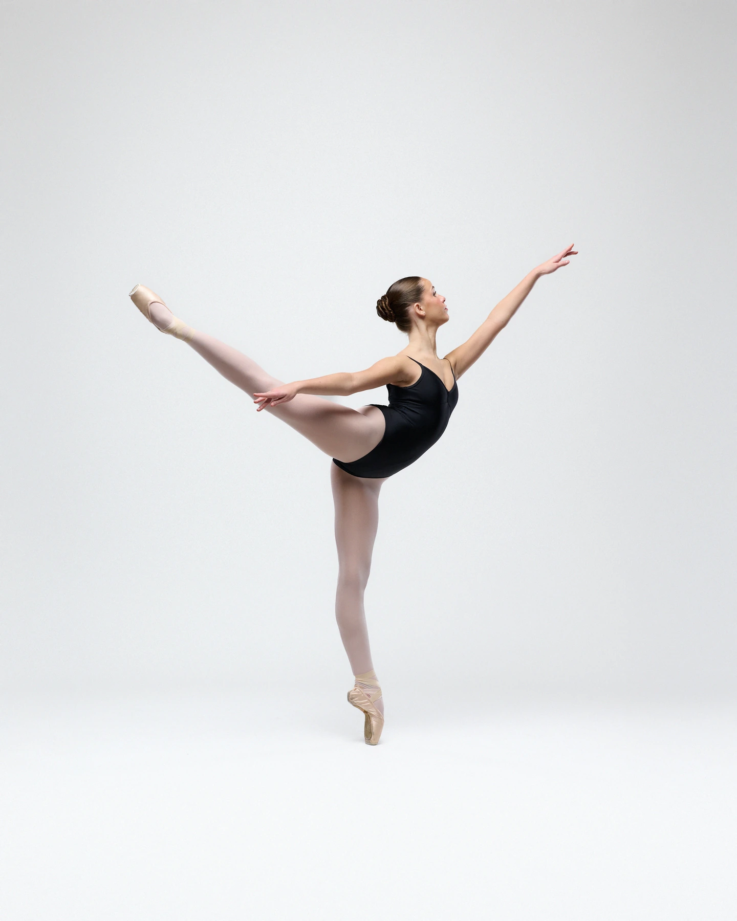 Ballerina extending a leg en pointe in a black leotard against white