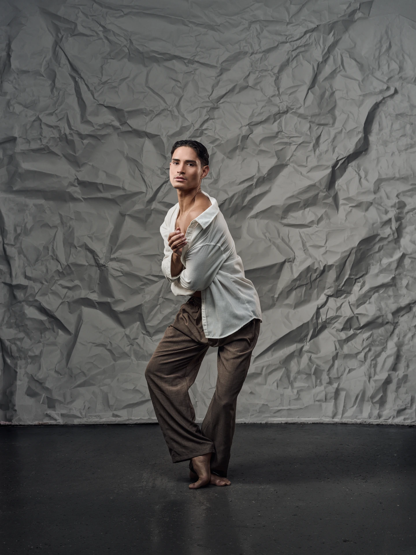 Dancer in a cream shirt and brown trousers against textured gray paper