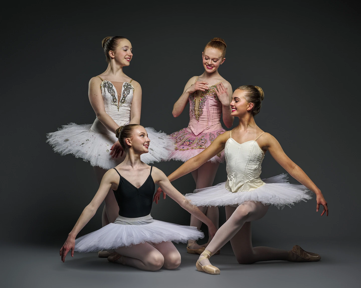 Four ballerinas in delicate tutus arranged against charcoal gray