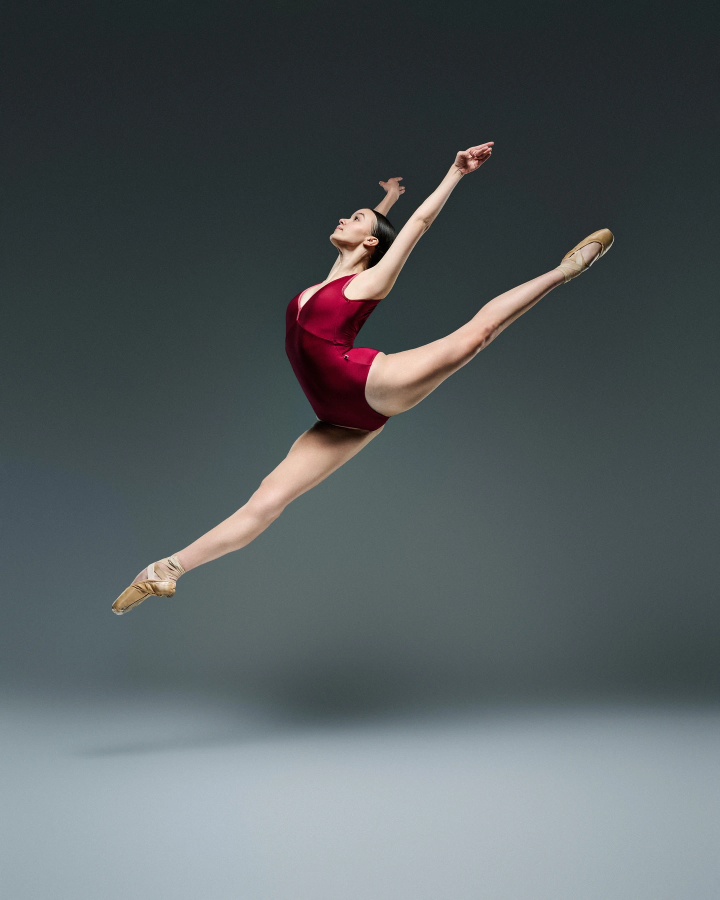 Ballerina in a red leotard captured in a split leap against cool gray