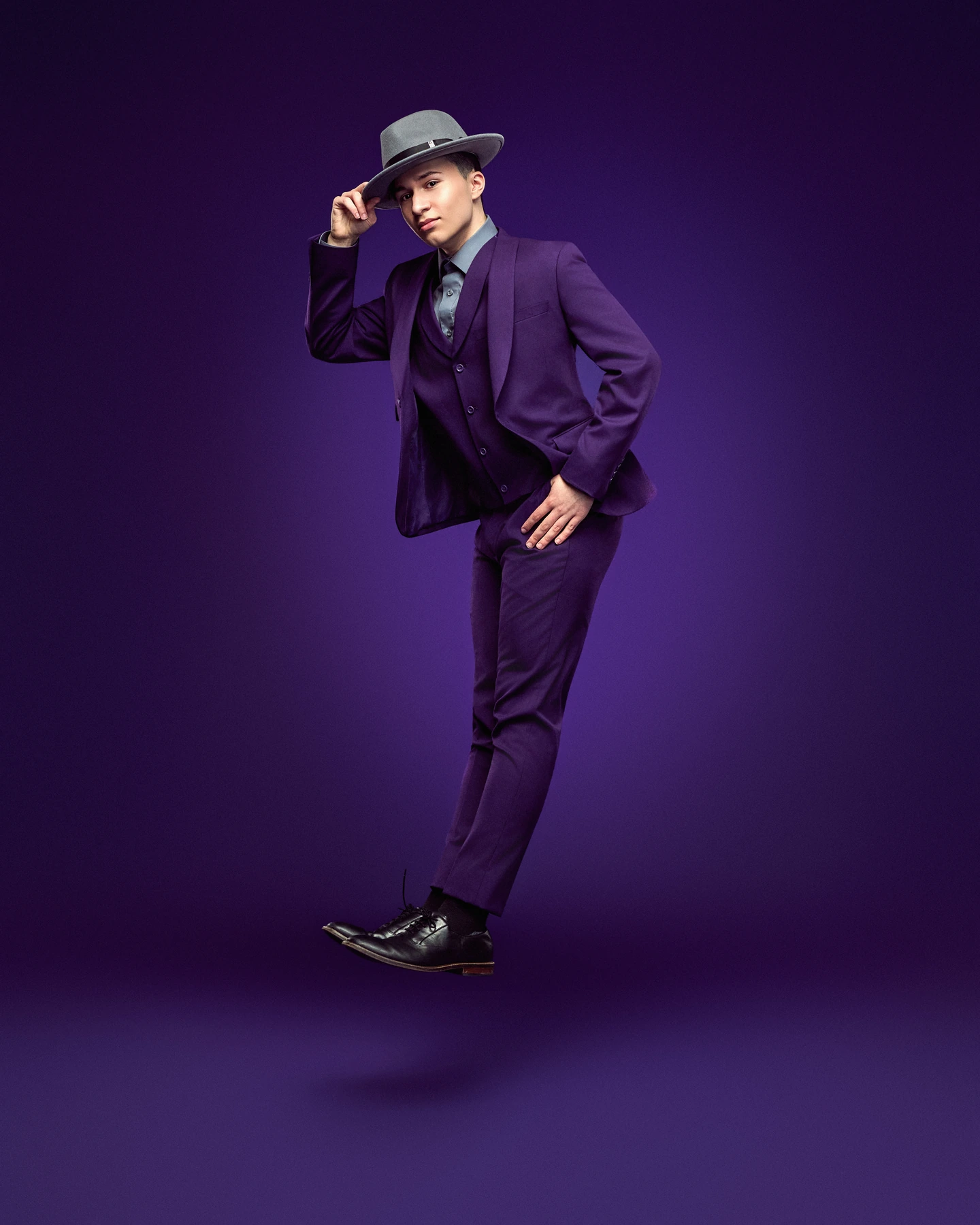 Dancer in a purple suit and gray hat suspended against purple