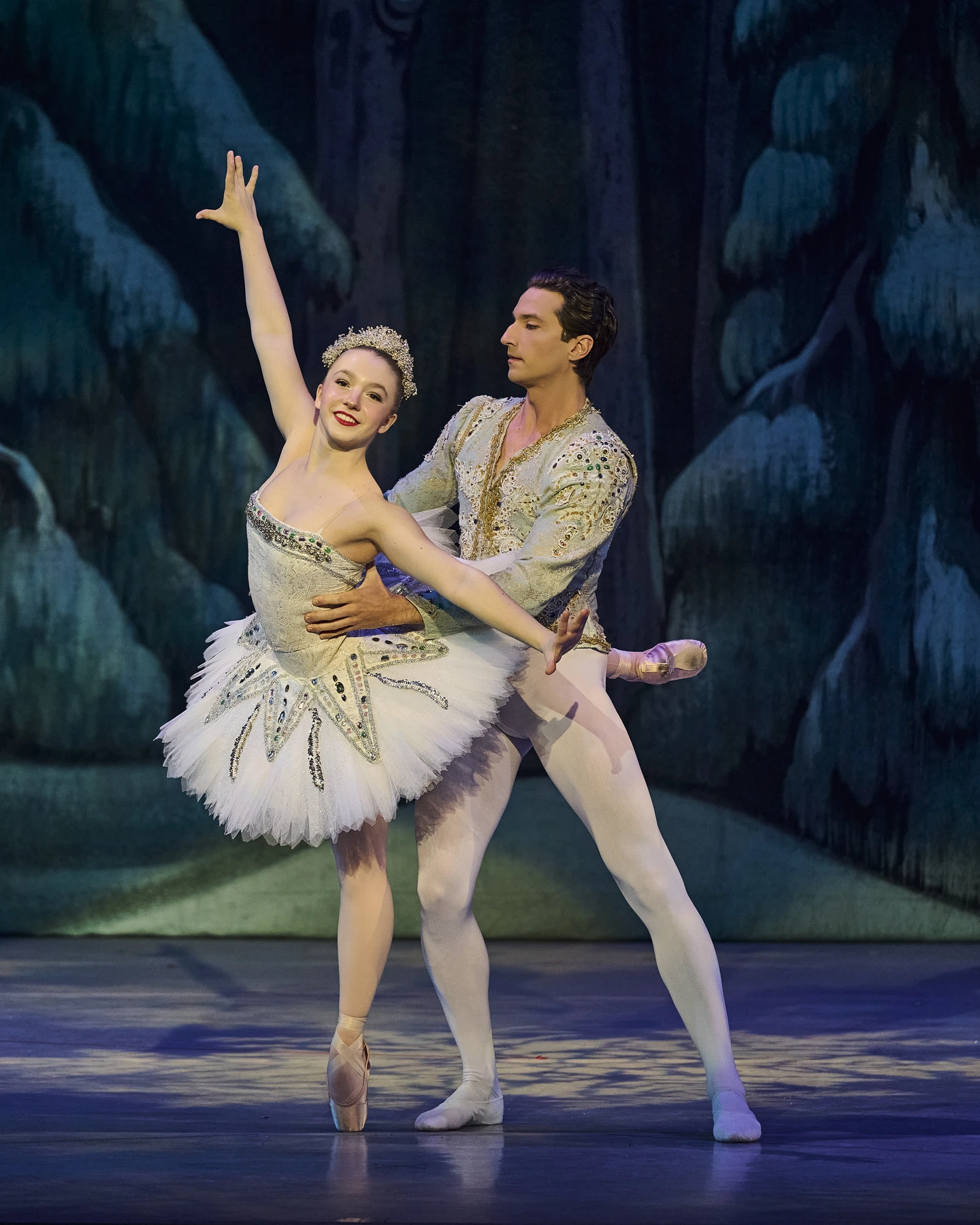 Ballet partners in ornate white costumes on a blue and teal stage