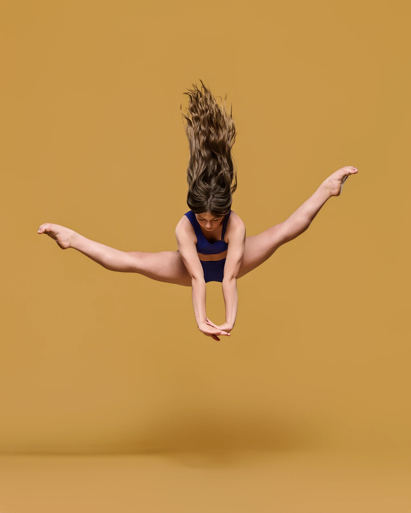Dancer in a straddle jump with flying hair against mustard yellow