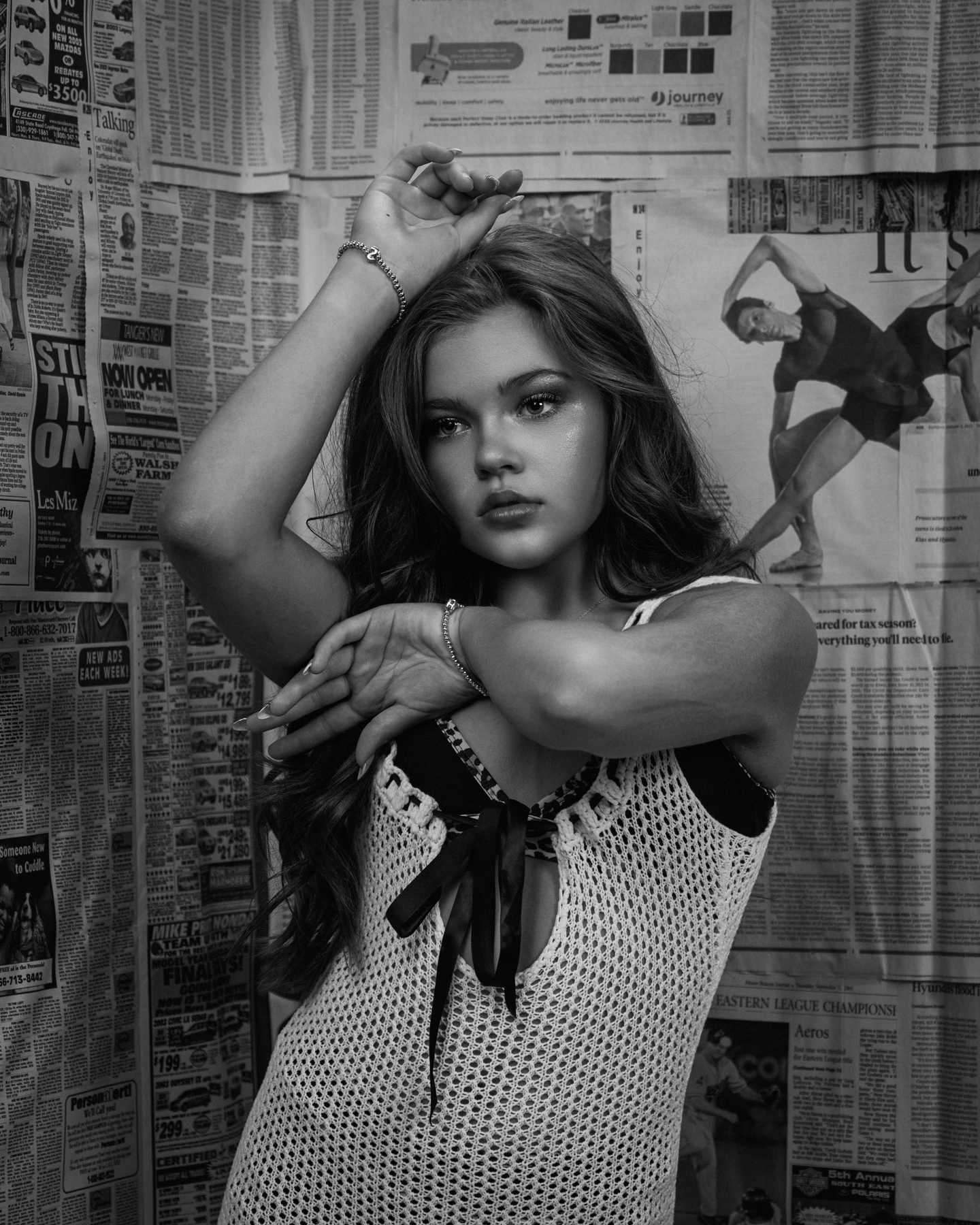 Black and white portrait with a raised arm against a newspaper wall