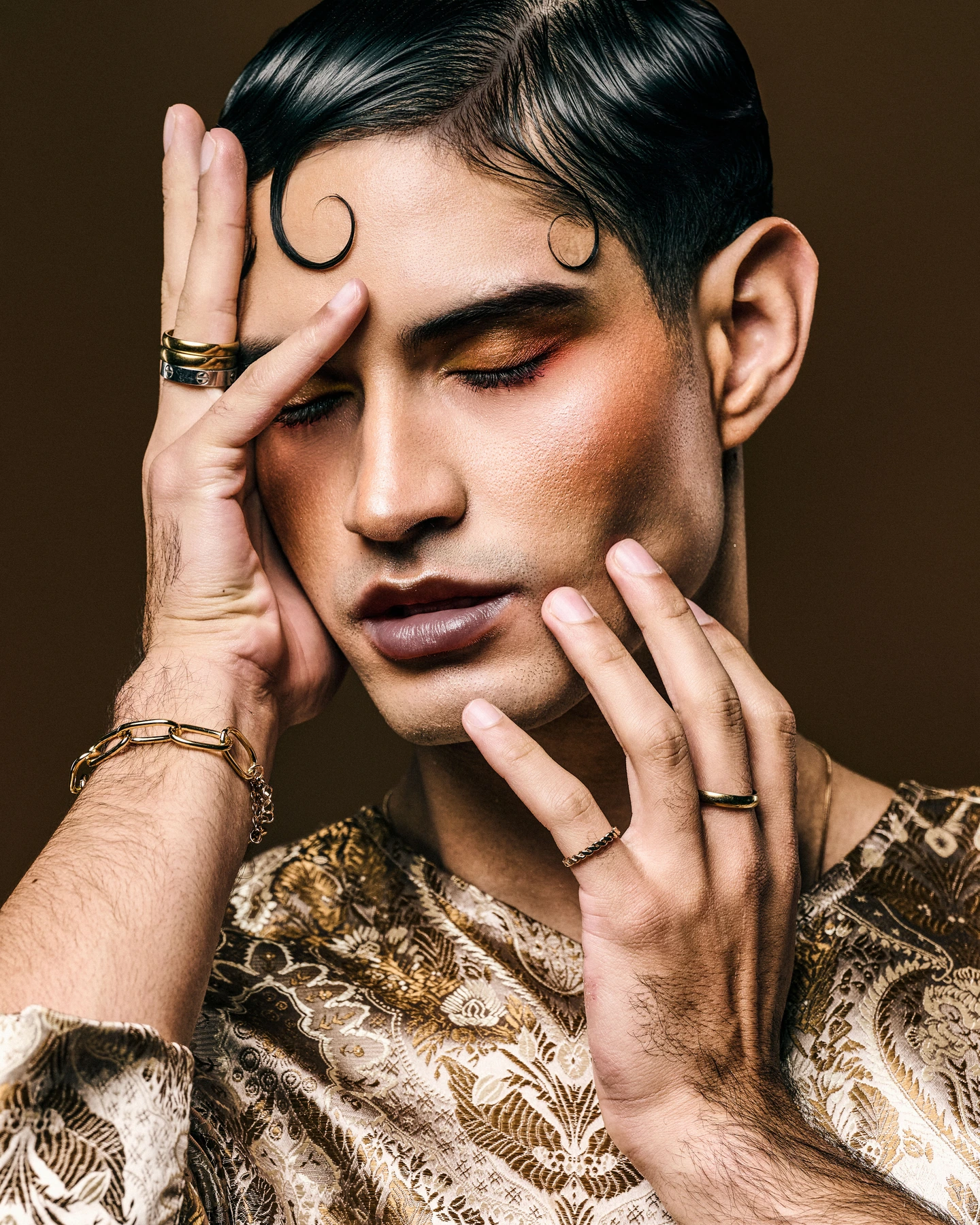 Close beauty portrait with gold makeup and jewelry against brown
