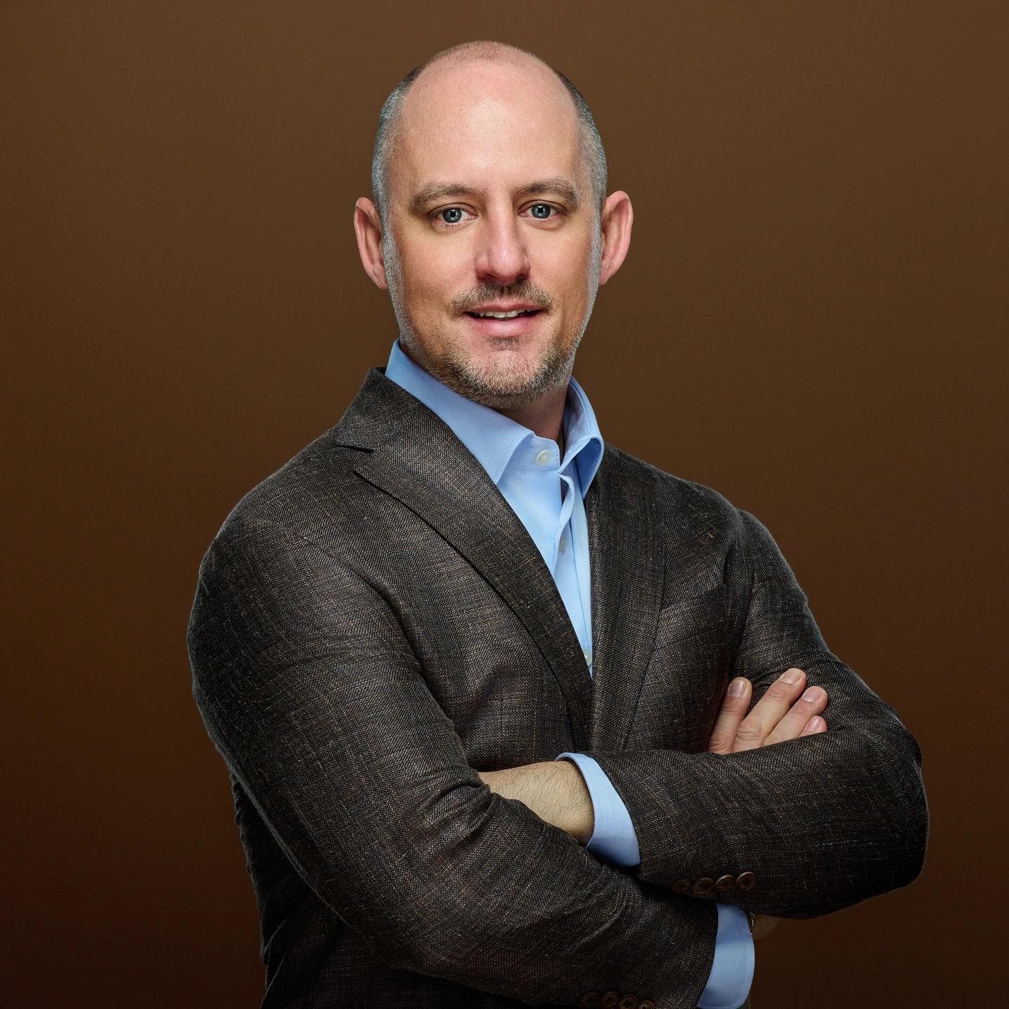 Business portrait in a dark jacket and blue shirt against brown