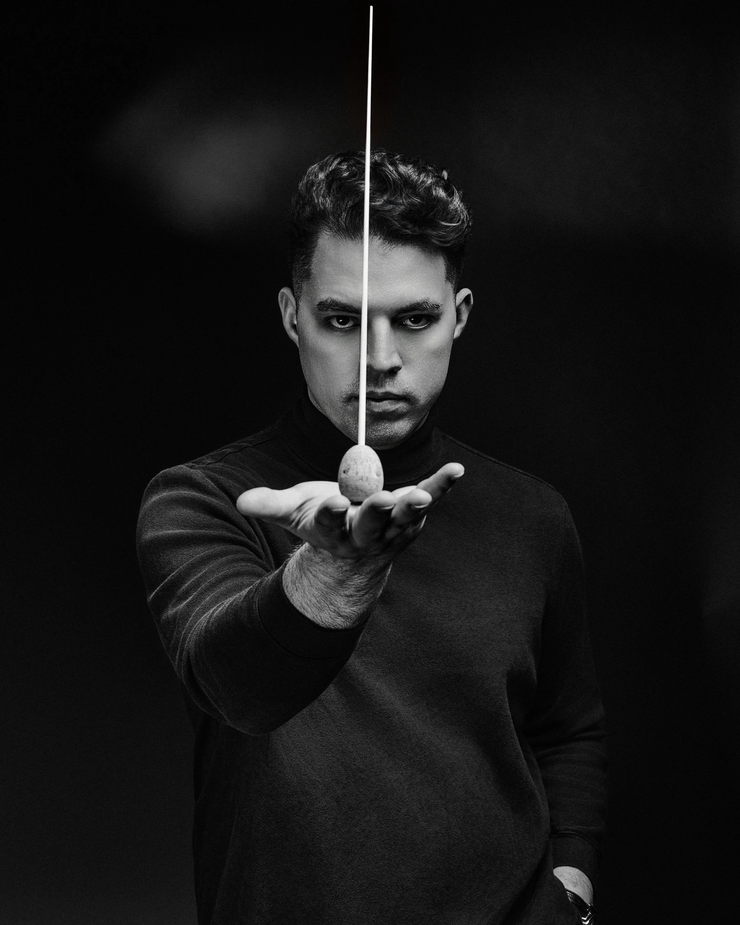 Black and white portrait with a conductor baton against black